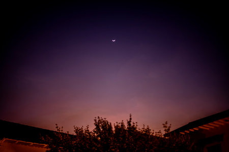 lonely moon with the crescent facing upwards on a purple sky and roofs in a black outlineの写真素材