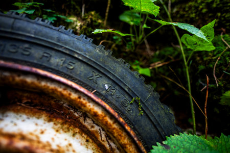 close-up of an old car wheel with a ruined black tire and rusty rim with peeling paintの写真素材