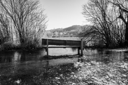abandoned and lonely wooden bench under the autumn trees among the frozen waters of Fimon lake in Vicenzaの写真素材