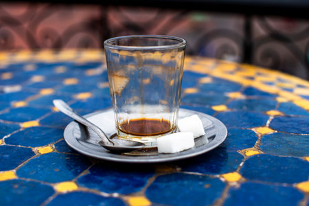 empty coffee glass with two sugar cubes a teaspoon metal saucer on decorated table in Marrackesh in Moroccoの写真素材