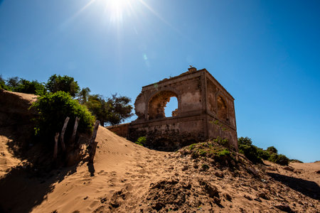ruins of ancient dwelling among the deserted dunes of the beaches with blue sky and green trees in...