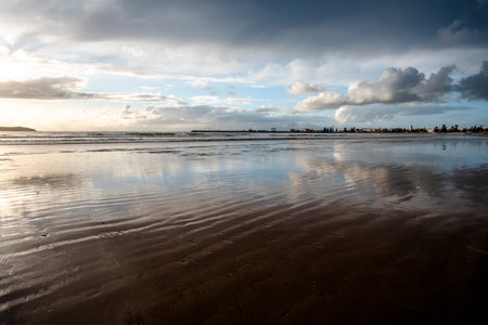 Sunset on the vast beaches of Essaouira with blue skies, white clouds and waves crashing on the...