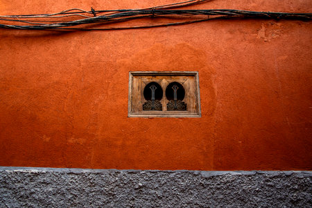 A rustic orange wall featuring an intricately designed wooden window and exposed electrical wires,...
