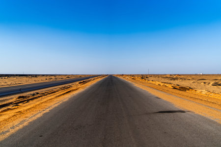 Straight desert highway stretching toward the horizon under a clear blue sky, conveying direction,...