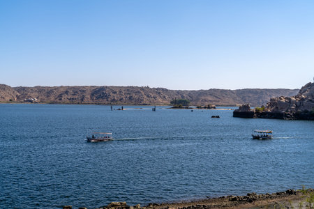 Passenger boats crossing the Nile in Aswan Egypt with rocky shoreline and open water introducing...