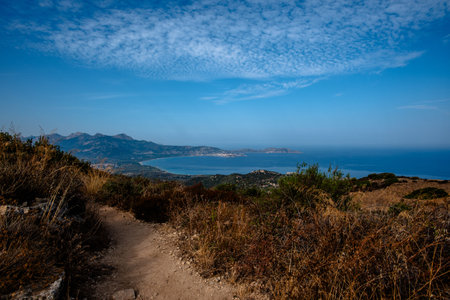 Wide view of a coastal bay and mountains seen from a hillside path near L'ÃŽle-Rousse, Corsica,...
