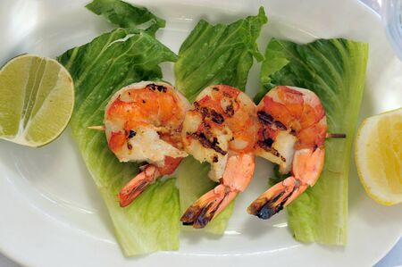 Jumbo shrimps on skewer with sweet garlic chili sauce on white plate with green lattice and lemon on a side の写真素材