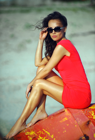 Glamour fashion model posing on the beach at the bouy wearing red dress and sunglasses.の写真素材