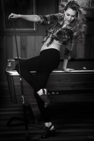 Young woman posing sexy in front of billiard pool table wearing leggins, shirt and red shoes