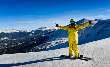 Snowboarder in bright yellow suit posing at the top of the mountain with scinic landscape on the background in Breckenridge, CO.の写真素材