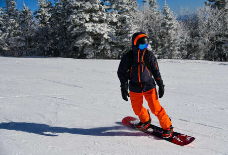 Young man snowboarder in bright outfit running down the slope. Winter sport and recreation, leisure outdoor activities.の写真素材