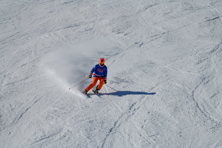 Skier in bright outfit skiing downhill on a sunny day in high mountains. Dynamic photo.