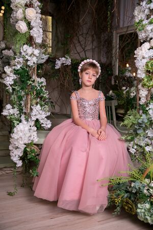 Little girl lady in pink dress and hat sits among magic flowersの写真素材