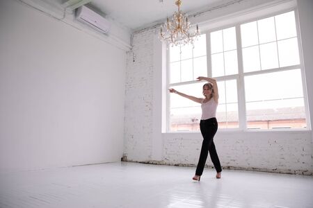 Portrait of young business woman black trousers pants isolated, In the white room loft by the big window, Goes and dances, raises handsの写真素材
