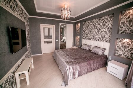 A grey bedroom with a bed and door. With chandelier, TV and bedside table.の写真素材