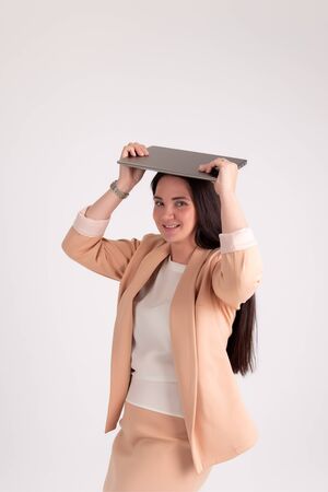 Successful business woman on grey background with copy space. Director in beige strict suit Keeps your laptop on your headの写真素材