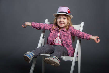 A little girl in a hat. smiles and laughs. gray background. In a pink shirt and grey pants. the childhood passes cheerfullyのeditorial素材