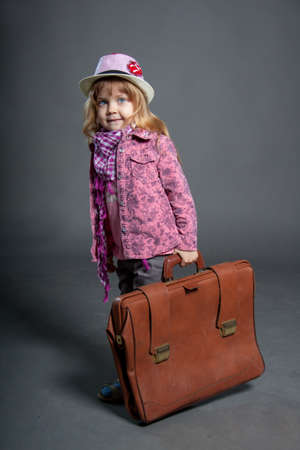 Little girl in hat holds big business suitcase for travelのeditorial素材