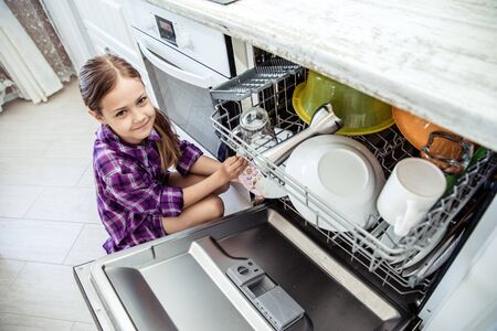 A dishwashing machine. The child clean dishes. the girl in kitchen. Little girl folding dishes in the dishwasher in the kitchenの写真素材