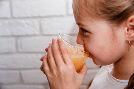 Beautiful little Girl drink fresh orange juice at kitchenの写真素材