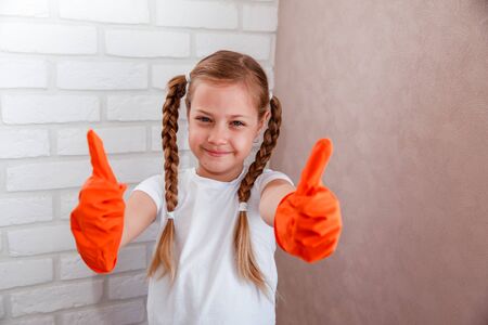 A little girl in orange gloves is cleaning the house.の写真素材