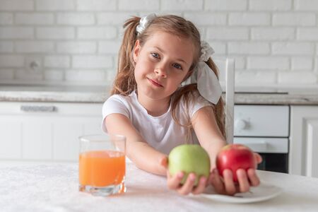little girl with juice and fruit apples in the kitchen. healthy food. vegetarianism. the child eats plant food. vitaminsの写真素材