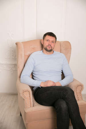 portrait of stylish man in eyeglasses sitting on wooden chair isolated on beigeの写真素材