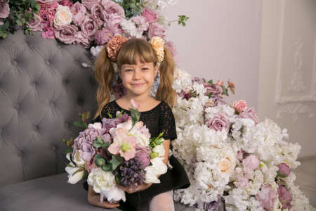 little girl holding a bunch of colouful flowers in her hands against a backdrop of closed curtains with copyspaceの写真素材