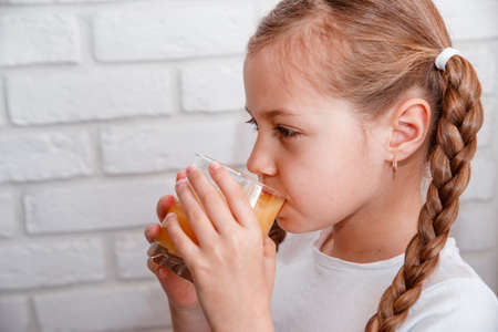 Beautiful little Girl drink fresh orange juice at kitchenの写真素材