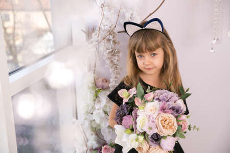 Beautiful little girl in black sleeveless top wearing cat ear headband and holding a bunch of flowersの写真素材