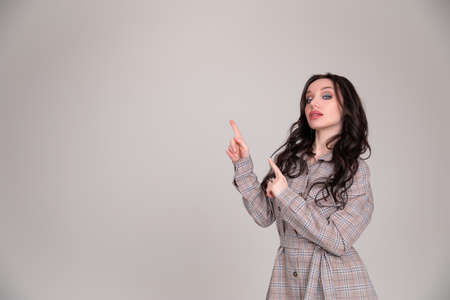 Beautiful young girl student, business woman smiles, pointing and looking away over gray backgroundの写真素材