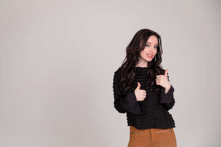 Beautiful young sexy girl smiles and showing the sign of approval. gray background. Copy space