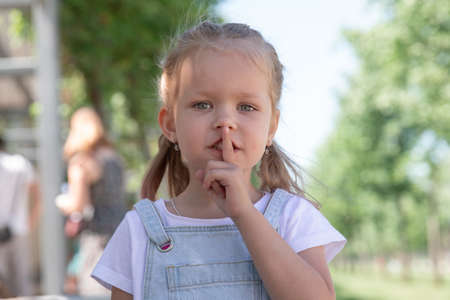 Closeup portrait of little girl holding her finger to her lips. quietly. do not make noise