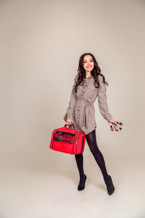 Model wearing stylish clothes & accessories. portrait of a beautiful young brunette with long hair. girl makeup artist holds a bag for makeup. Copy spaceの写真素材