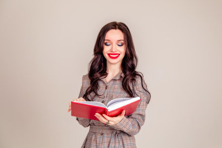 a beautiful young girl with red lips holds a red notebook in her hands. student. businesswoman on isolated gray background. education. Copy spaceの写真素材