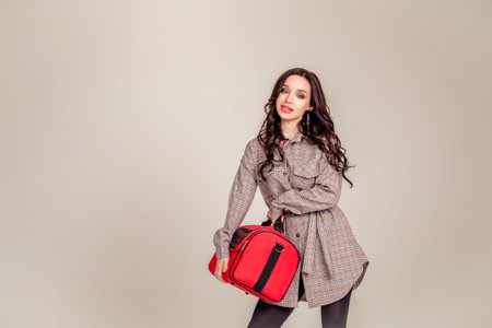 Model wearing stylish clothes & accessories. portrait of a beautiful young brunette with long hair. girl makeup artist holds a bag for makeup. Copy spaceの写真素材