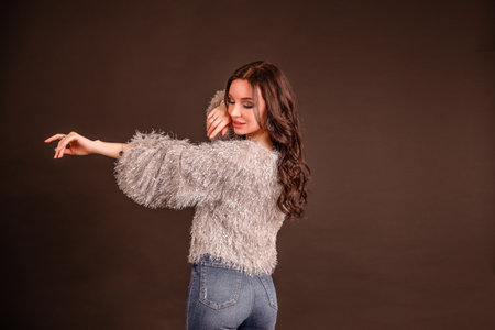 portrait beautiful girl poses on a black gray background. lady in jeans and gray fluffy sweater. view from the back. beautiful popの写真素材
