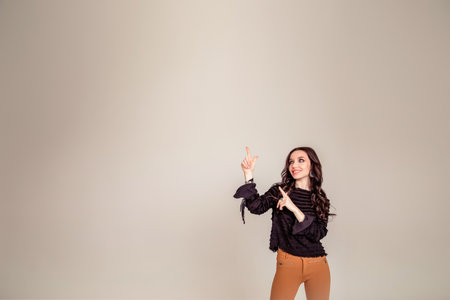 Portrait with copy space for advertisement of attractive, amazed, stylish, impressed, funny girl pointing forefinger to empty place isolated on gray backgroundの写真素材