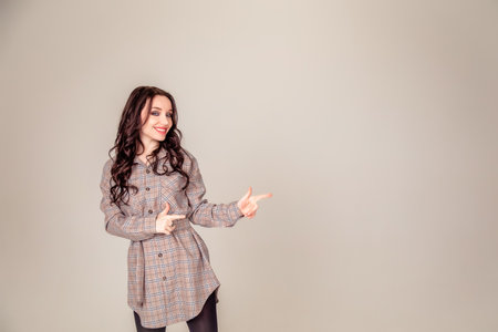 Smiling portrait of a beautiful young brunette with long hair. businesswoman pointing and looking away over gray background. Copyspaceの写真素材