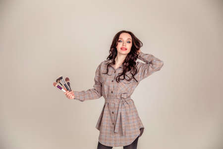 portrait of a beautiful young brunette with long hair. girl makeup artist holds makeup brushes in her hands. Beauty club concept. Copy spaceの写真素材