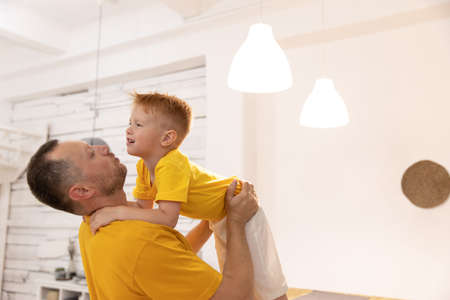 father and little son playing funny game at home, loving happy dad carrying adorable preschool boy pretending flying with hands outstretched, lying on cozy couch in living room. male parent holds a boy in outstretched armsの写真素材