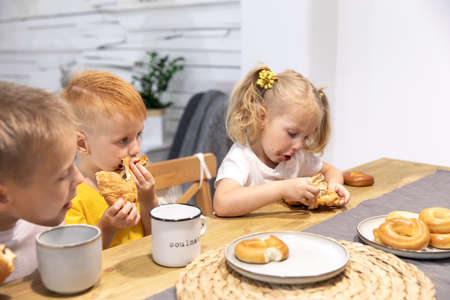 a little red boy and a little girl eat croissants. the kids got dirty in chocolate. brother and sister have breakfastの写真素材