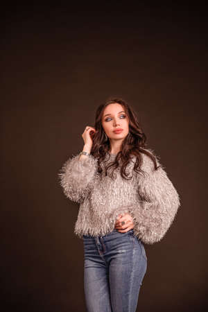 portrait beautiful girl poses on a black gray background. lady in jeans and gray fluffy sweaterの写真素材
