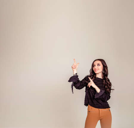 Portrait with copy space for advertisement of attractive, amazed, stylish, impressed, funny girl pointing forefinger to empty place isolated on gray backgroundの写真素材