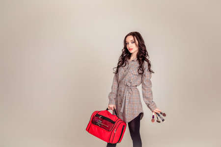 Model wearing stylish clothes & accessories. portrait of a beautiful young brunette with long hair. girl makeup artist holds a bag for makeup. Copy spaceの写真素材