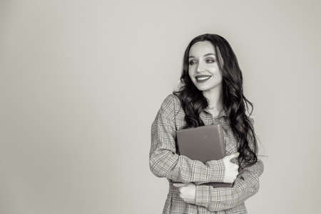 a beautiful young girl with red lips holds a red notebook in her hands. student. businesswoman on isolated gray background. the concept of education. Copy space. Black-white photoの写真素材
