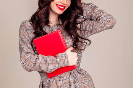a beautiful young girl with red lips holds a red notebook in her hands. student. businesswoman on isolated gray background. the concept of education. Copy spaceの写真素材