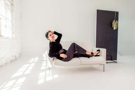 Sexy beautiful business woman lady boss manager secretary. portrait of a sexy beautiful brunette in a black suit on a white sofa. copyspace. Tonedの写真素材