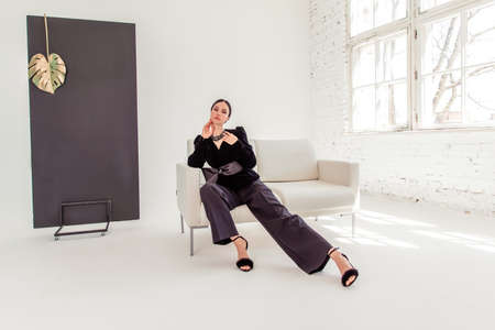 sexy businesswoman in a suit in a white photo studio. woman sitting on a white sofa. copyspace. Toned.の写真素材