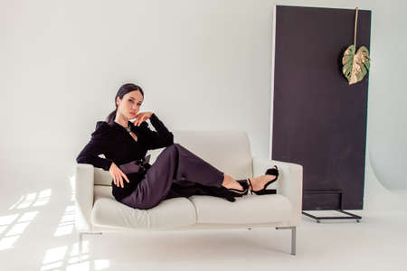 Sexy beautiful business woman lady boss manager secretary. portrait of a sexy beautiful brunette in a black suit on a white sofa. copyspace. Tonedの写真素材